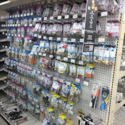 Store aisle with a pegboard wall displaying neatly organized plumbing fittings in plastic packaging. The shelf conveys a sense of order.