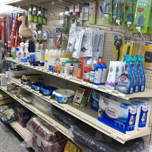 Pet store aisle with shelves displaying various products including dog food, treats, toys, grooming supplies, and pet care items. A diverse and colorful selection.