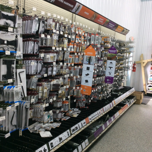 A hardware store aisle with various gate and home hardware items, including hinges and handles, neatly organized on a perforated display wall.