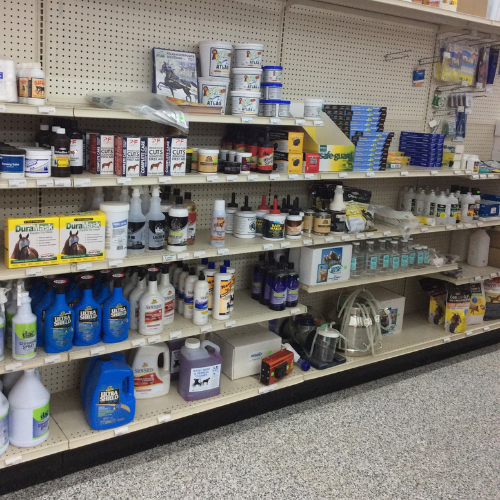 Shelves filled with various horse care products, including sprays, ointments, and supplements, in a well-lit store. Tone conveys organization and variety.