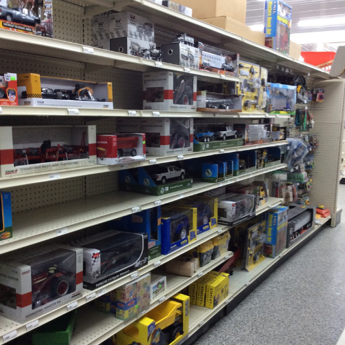 Store aisle with shelves filled with boxed toy trucks and cars, neatly organized. Bright lighting gives a clean, inviting atmosphere.